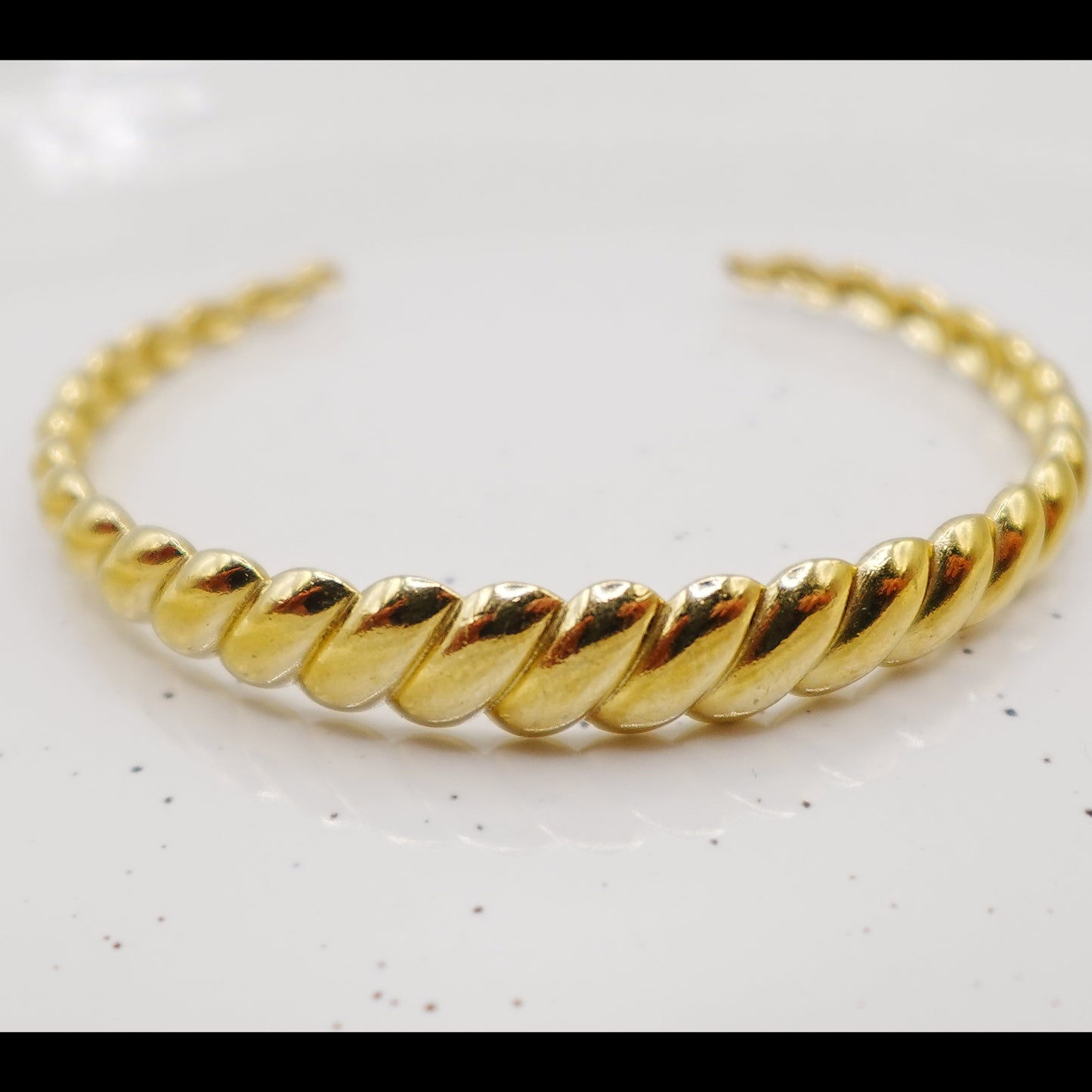 Gold braided bracelet on a light gray background