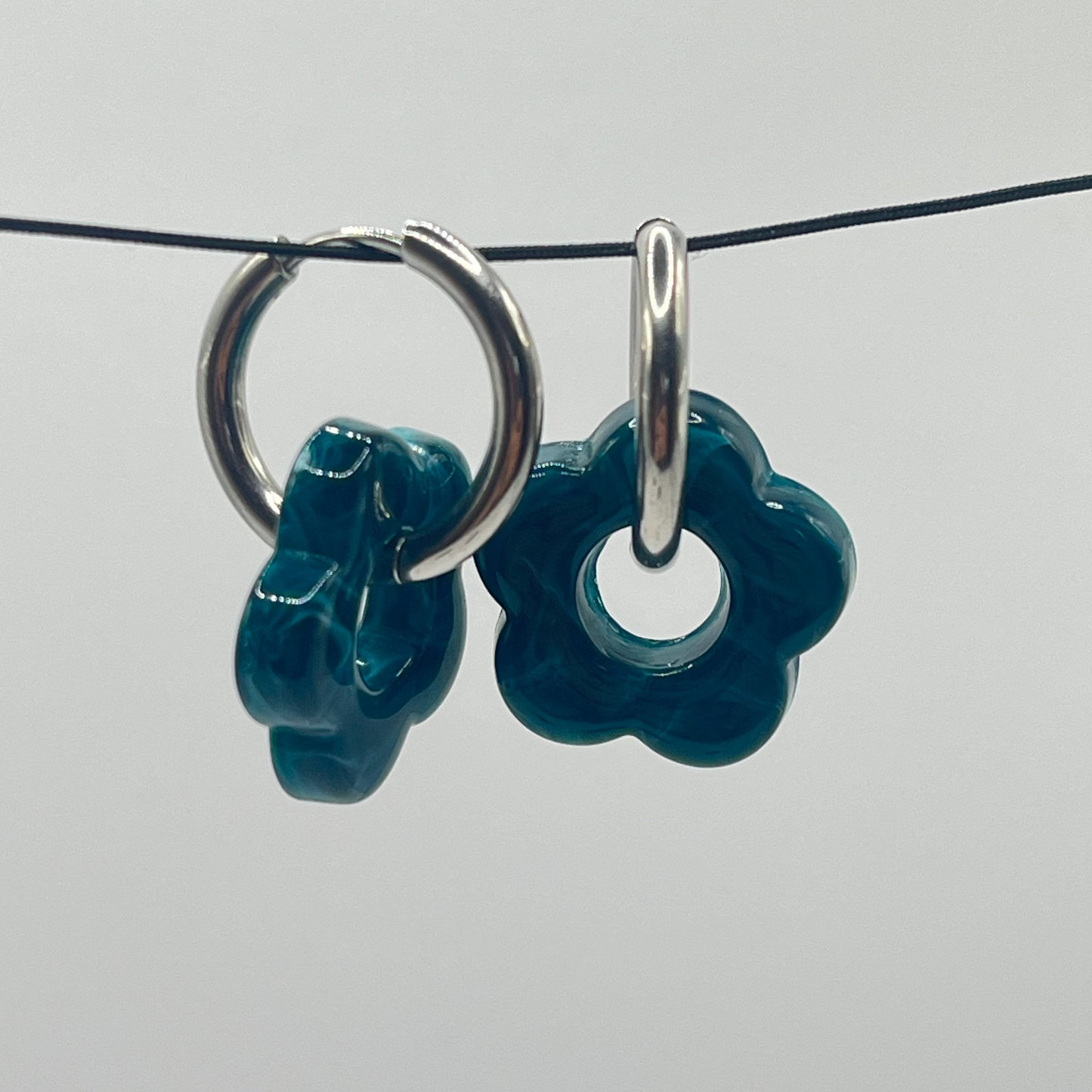 Teal flower-shaped earrings with silver loops on a gray background