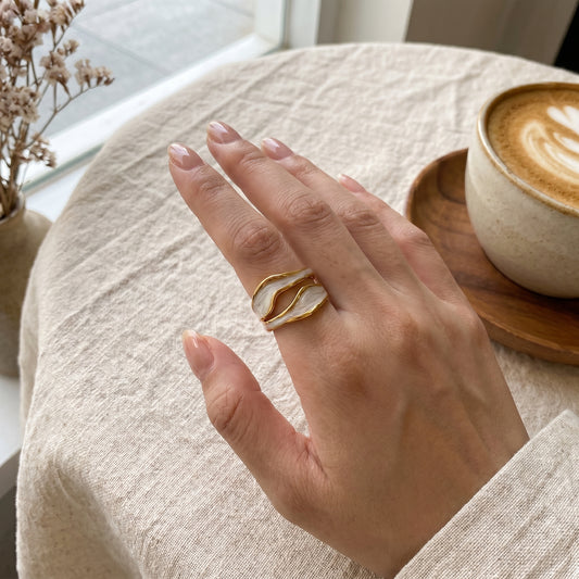 Hand wearing a gold ring with a cup of coffee and dried flowers in the background