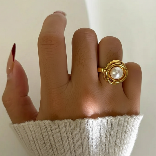 Hand wearing a gold ring with a pearl on a plain background