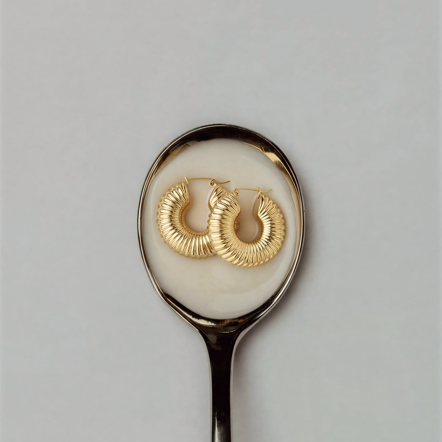 Gold hoop earrings on a silver spoon with a white background