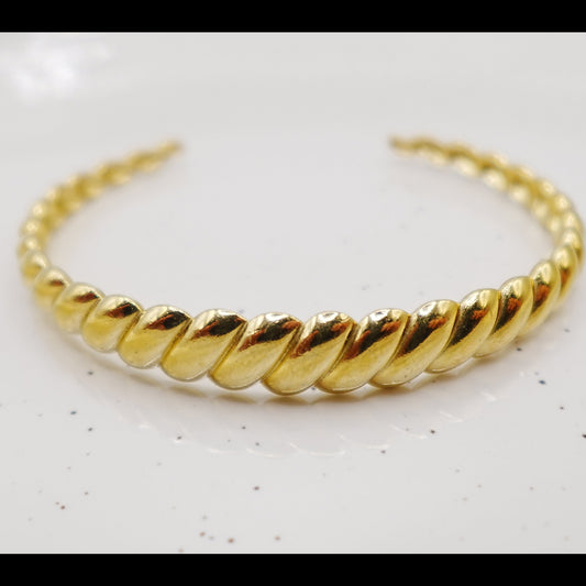 Gold braided bracelet on a light gray background