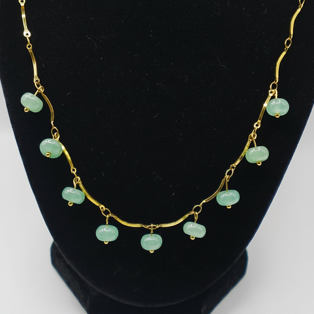 Necklace with green beads on a black stand against a white background