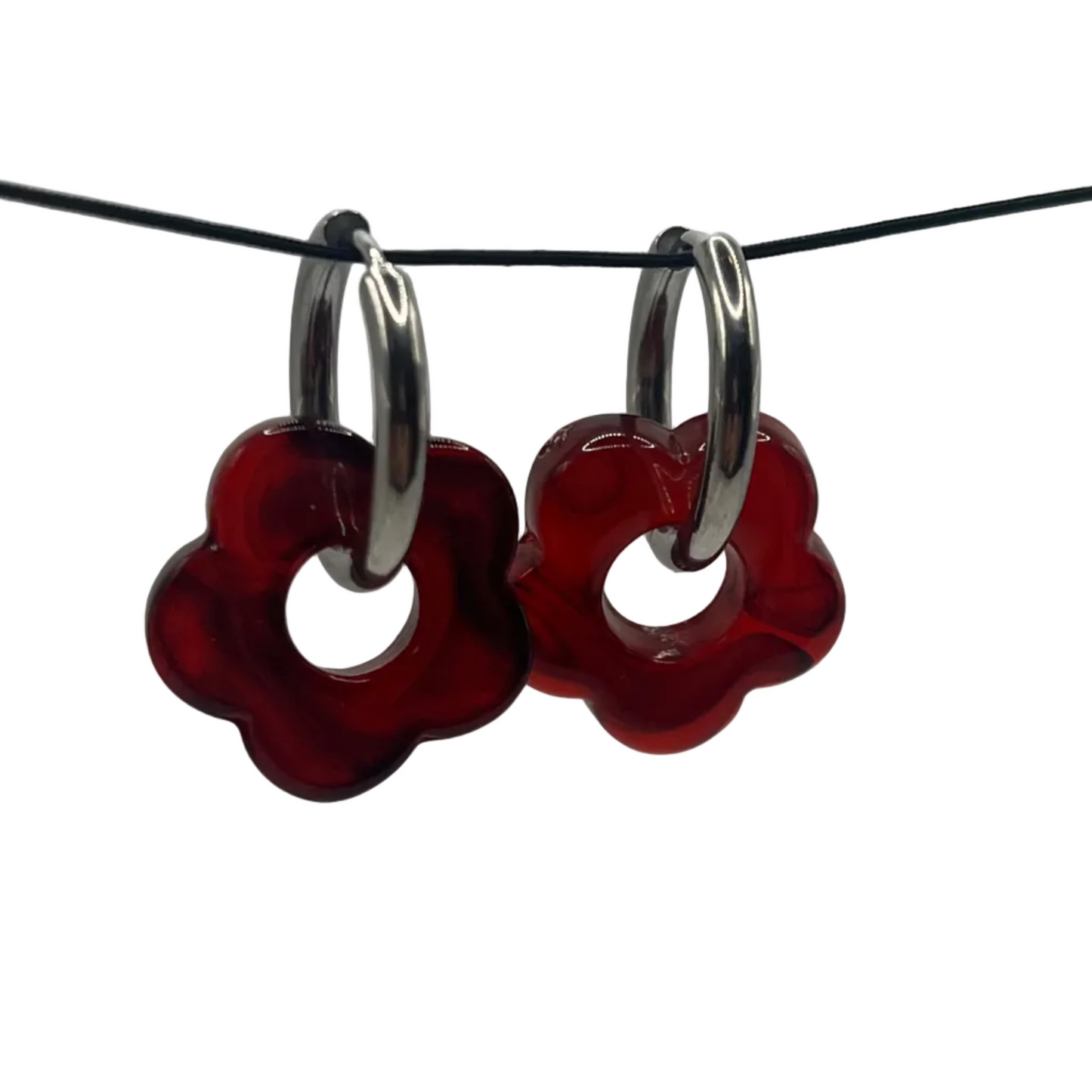 Red flower-shaped earrings with silver loops on a black wire against a gray background