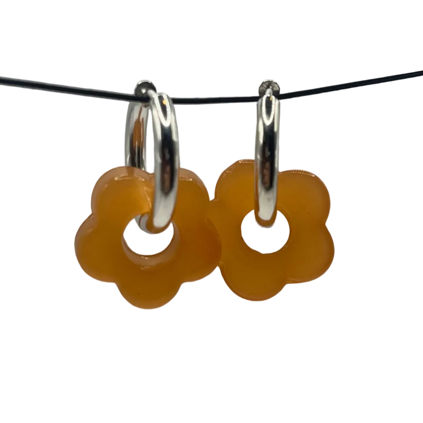 Pair of yellow flower-shaped earrings on a black cord against a gray background