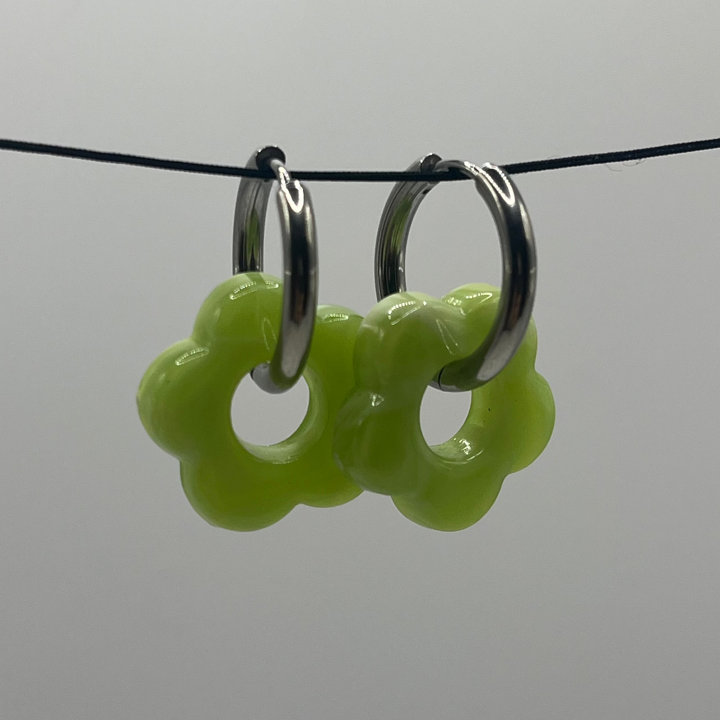 Bright Green floral hoop earrings on a black cord against a light gray background