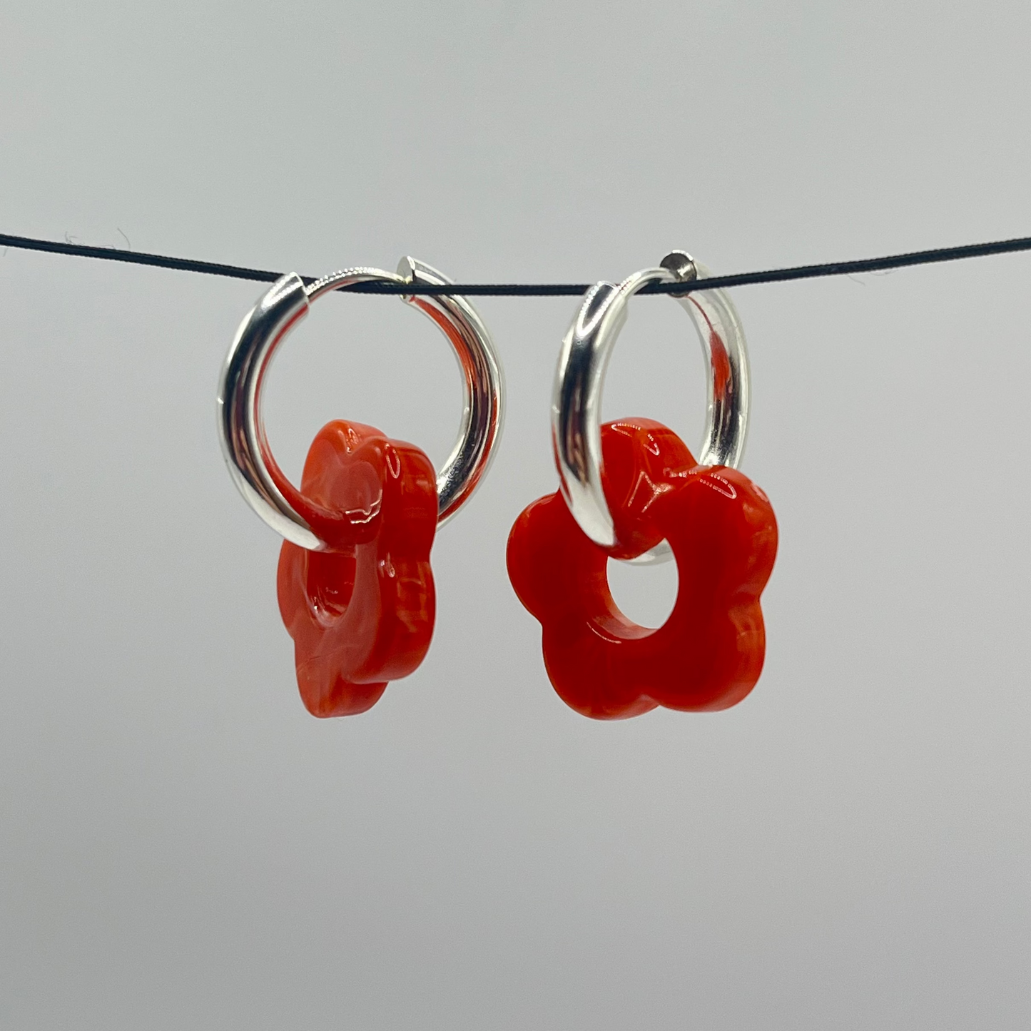 Pair of orange floral hoop earrings on a thin black wire against a light gray background