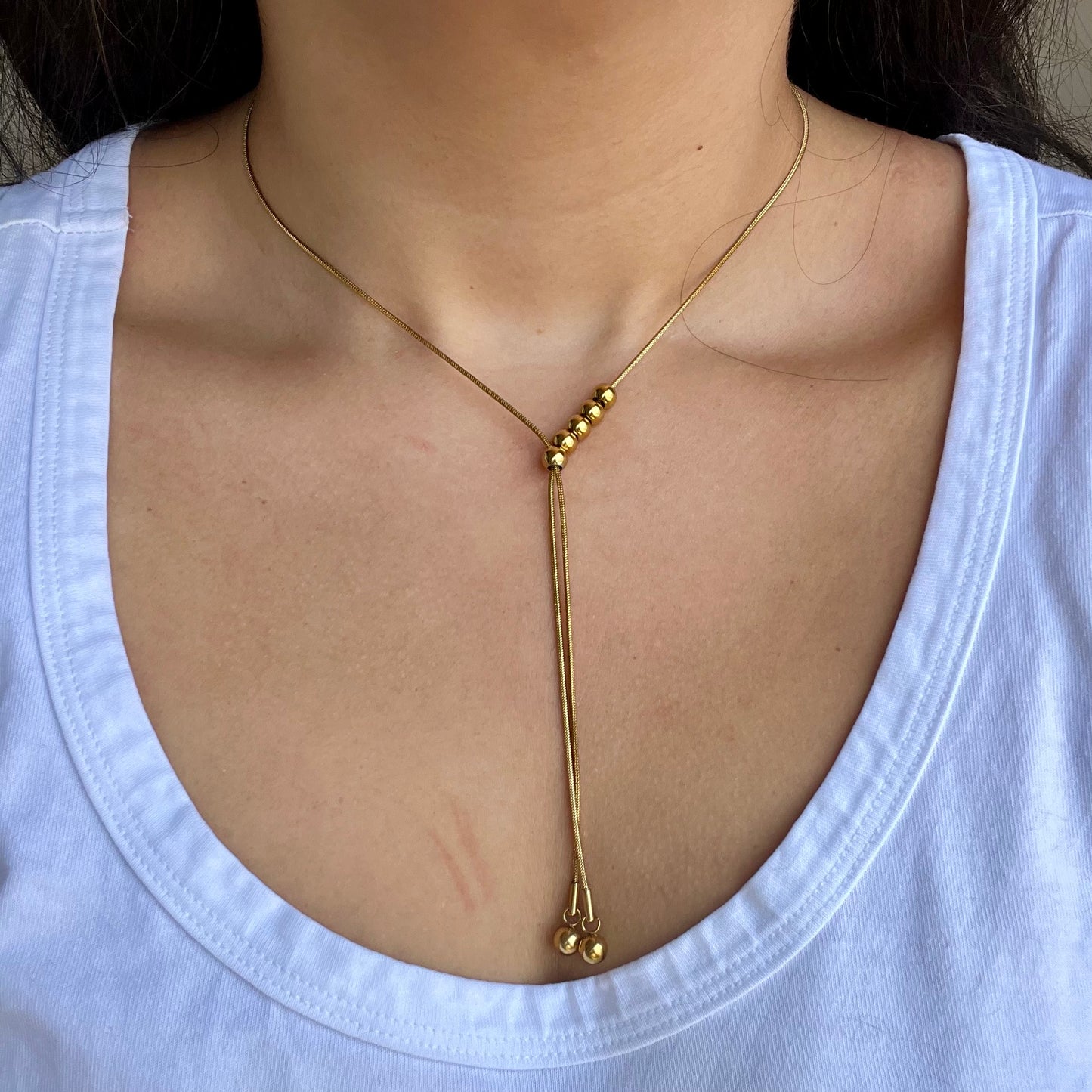 Gold necklace with beads on a person wearing a white top