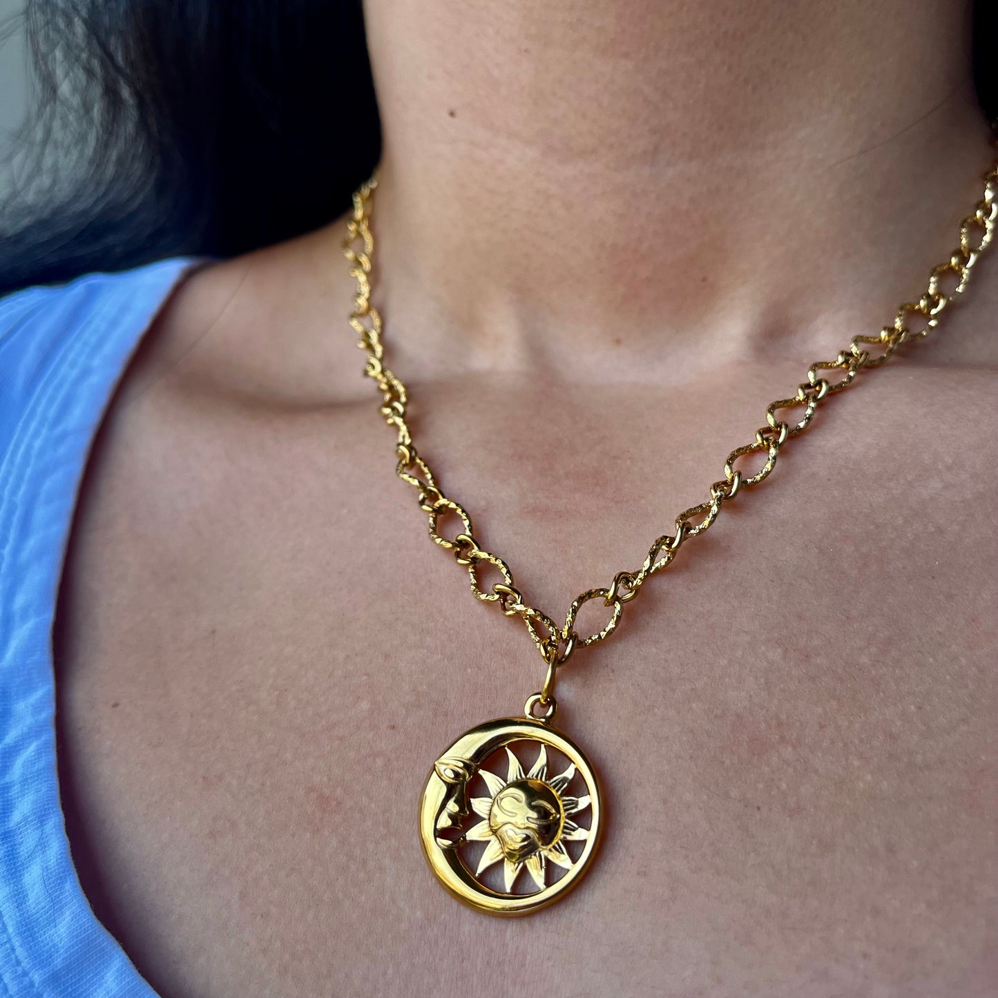 Gold chain necklace with a sun and moon pendant worn by a person.