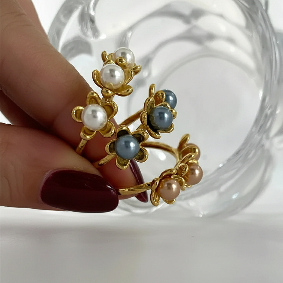 Gold ring with pearls and gemstones held by a hand against a clear glass background