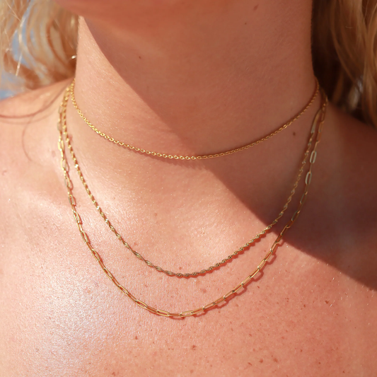 Three gold necklaces layered in a woman's neck