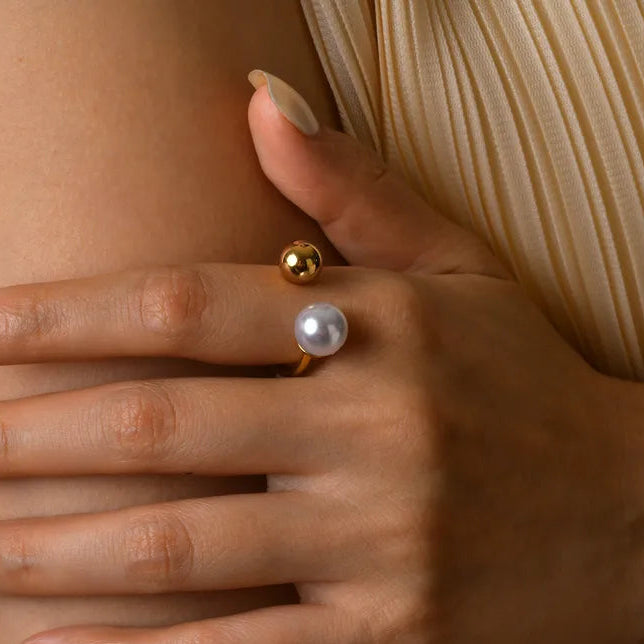 Close-up of a hand wearing two pearl earrings against a neutral background
