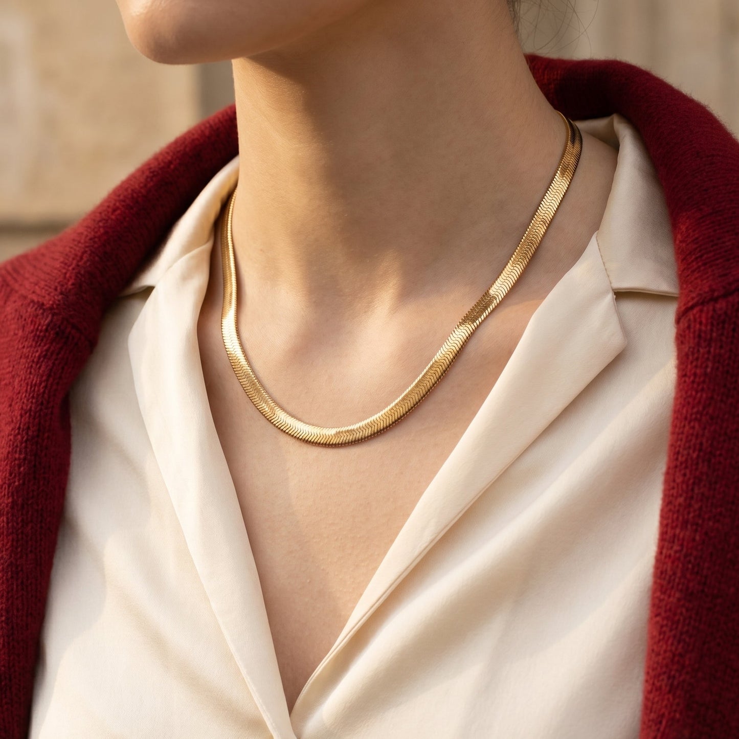 Person wearing a gold necklace with a red cardigan and white shirt, featuring the brand 'NORU'.