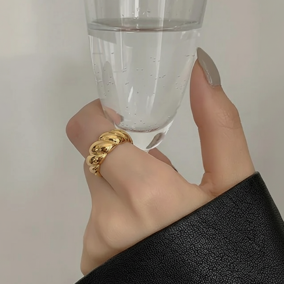 Hand holding a clear glass with a gold ring on a neutral background