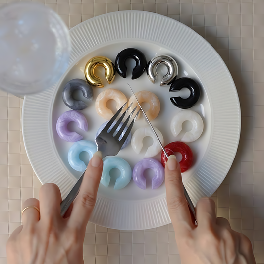 Colorful ear cuffs on a white plate with hands using a fork to pick them up.