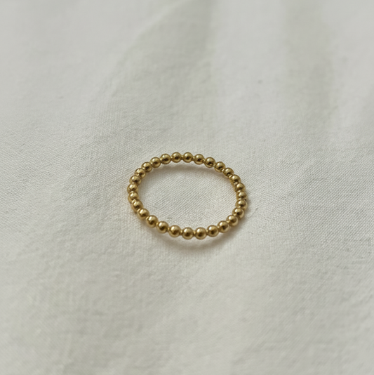 Gold beaded ring on a white fabric background