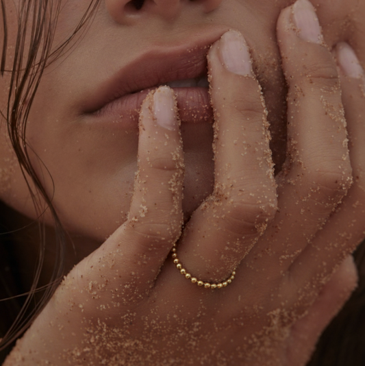 Close-up of a hand with sand on it touching a person's face, wearing a gold ring.
