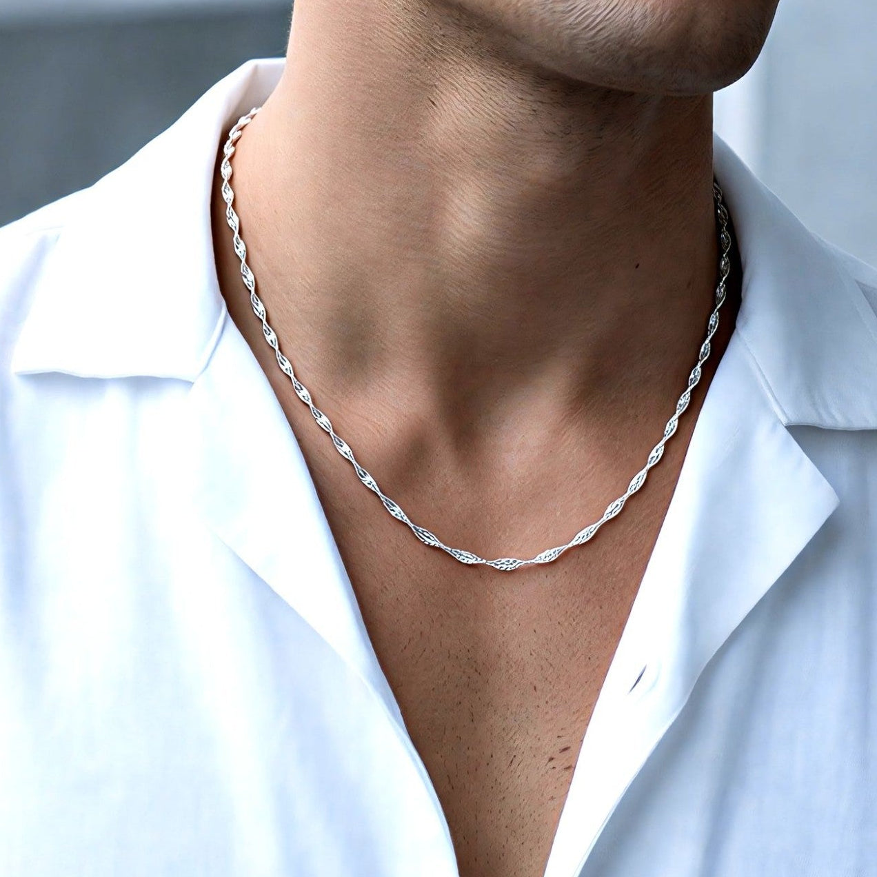 Man wearing a white shirt and silver necklace with a blurred background