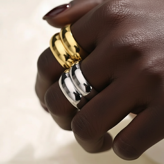 Hand wearing two gold rings on a neutral background