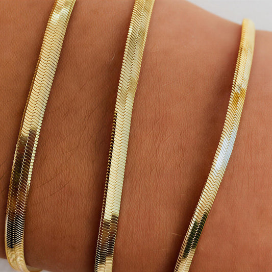 Gold bracelet on a wrist with a plain background