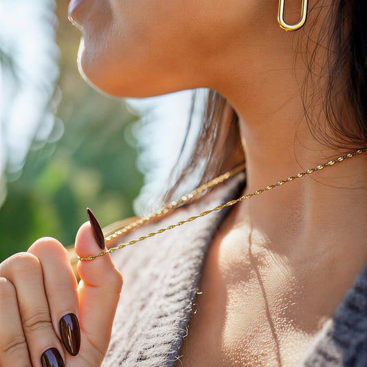 Close-up of a person wearing a gold necklace with a blurred natural background